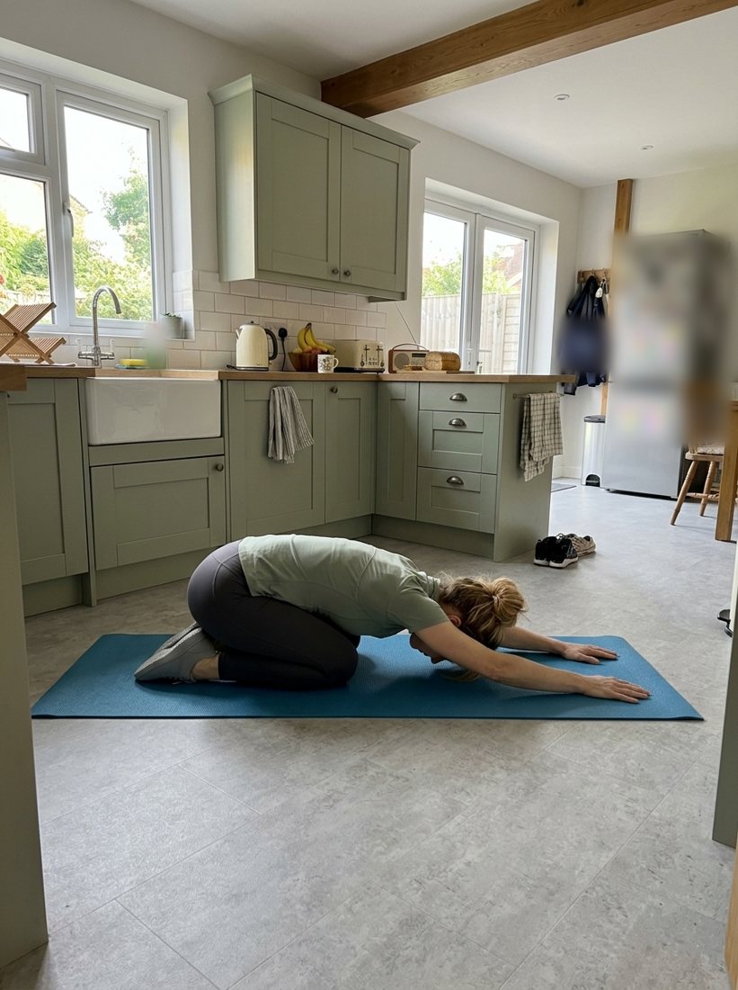 Claire resting in child's pose on a blue mat on the kitchen floor